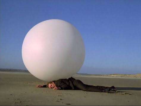 a picture of the tv series The Prisoner where the protagonist is lying on the beach with a big white ball on him